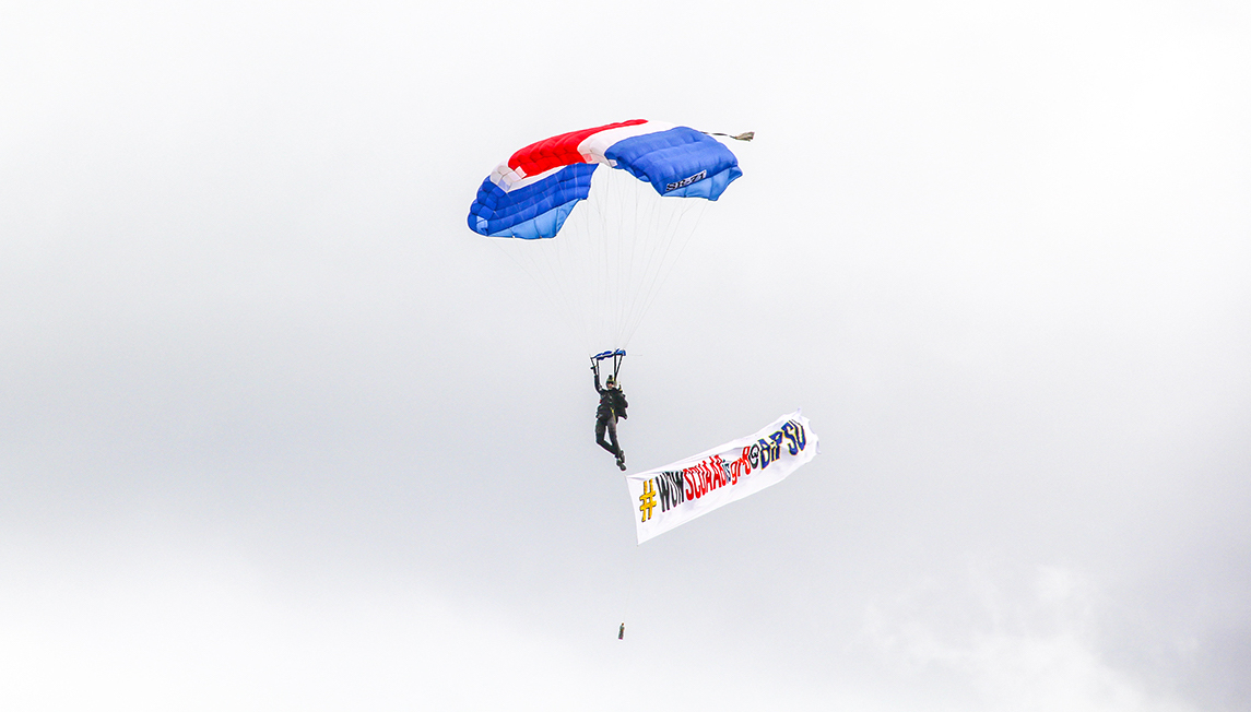 EXHILARATING. A skydiver carries a banner to welcome delegates reading "#WOWSCUAAisgr8@BiPSU" a few minutes before the parade begun.